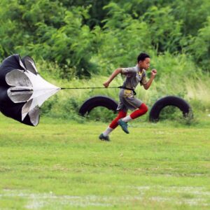 Energetic young boy runs in a grassy field with a training parachute, showcasing athleticism and determination.