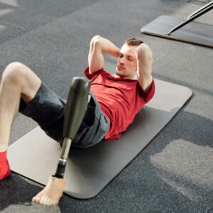 Man performing sit-ups on yoga mat using prosthetic leg in fitness gym.