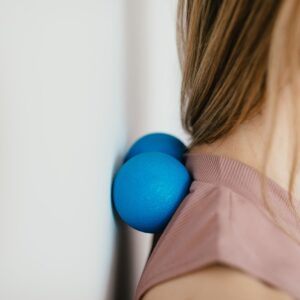 Side view crop unrecognizable female leaning on small balls against wall to massage stiff neck muscles and sore neck