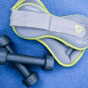 From above of modern dumbbells and leg weight belts placed on blue fitness mat in studio