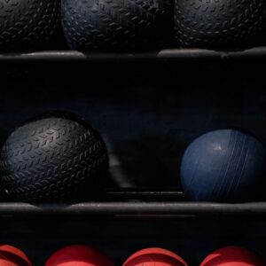 Array of black, blue, and red exercise balls neatly arranged in a gym setting.