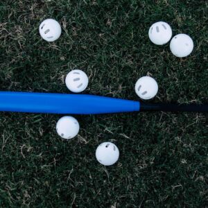 A blue baseball bat surrounded by white practice balls lying on green grass outdoors.