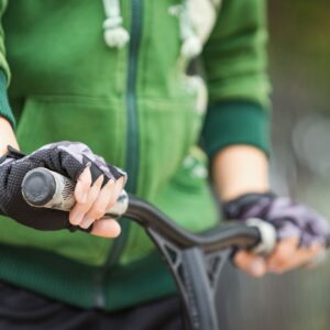 A person wearing gloves rides a scooter, focusing on the handle bars.
