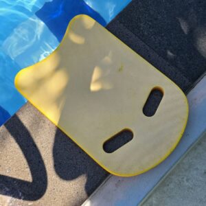 A yellow kickboard sits beside a pool.